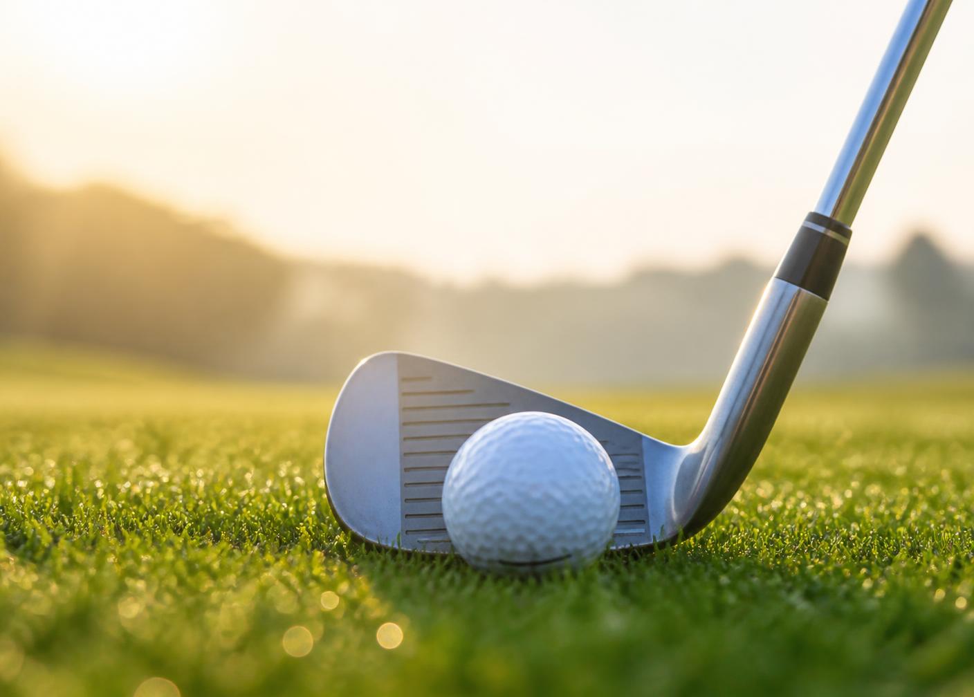 Golfová hůl u míčku na trávě v podvečerním světle